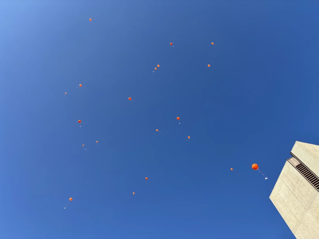 Orange Luftballons, die über dem Gemeindegrundstück an der Marchlewskistraße in den Himmel steigen.